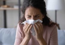Hospital Chiefs Brace — 2025 Flu Outlook Darkens Woman sneezing into a tissue indoors.