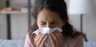 Hospital Chiefs Brace — 2025 Flu Outlook Darkens Woman sneezing into a tissue indoors.