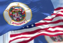 Minneapolis Meltdown Over Sudden Immigration Crackdown Minnesota state flag with American flag in background.