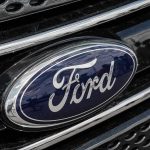 $19.5B EV Gamble BLOWS UP Ford logo on car grille close-up.
