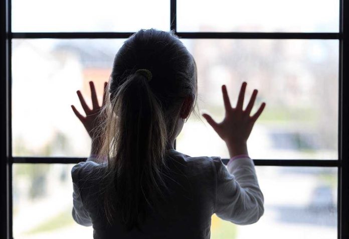 shutterstock_189988664.jpg A child with long hair presses their hands against a window, looking outside