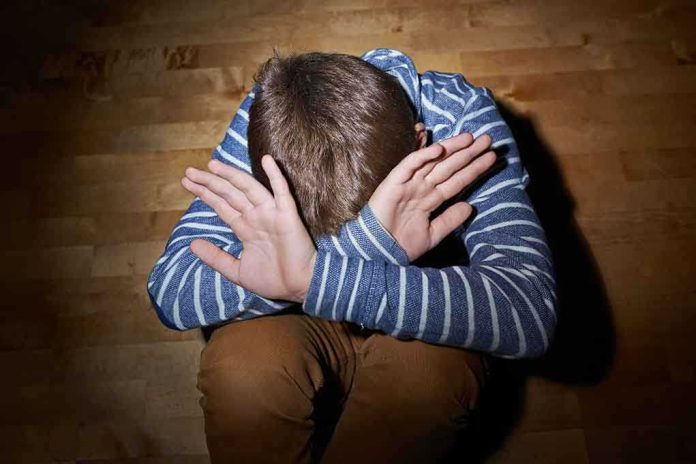 shutterstock_237679426.jpg A child sitting on the floor with their hands covering their face, expressing distress