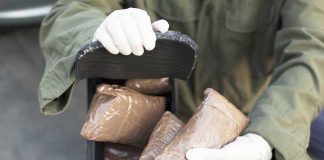 U.S. ESCALATES Drug War Person handling packages wearing gloves and green jacket.