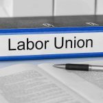 Blue binder labeled Labor Union beside papers and pen.