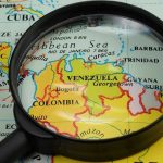 U.S. Forces Capture Venezuelan Dictator Magnifying glass focusing on Venezuela and Colombia on map.