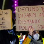 Two individuals holding protest signs with messages about police reform