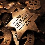 Sheriff Deputy’s Dark Secret A collection of vintage sheriff badges arranged on a dark surface