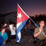 Cuba Plunges Into Darkness A group of people participating in a protest march holding a Cuban flag