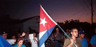 Cuba Plunges Into Darkness A group of people participating in a protest march holding a Cuban flag
