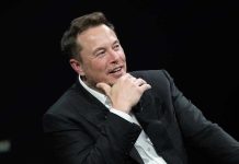 Musk Exposes Judge Bias Bomb Man in suit smiling, resting chin on hand.