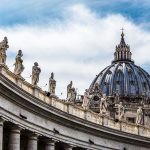Church Doctrine Under Fire – Who’s Behind It? St. Peters Basilica dome with statues and clouds.