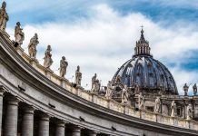 Church Doctrine Under Fire – Who’s Behind It? St. Peters Basilica dome with statues and clouds.