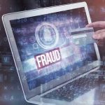 Person holding credit card near laptop displaying Fraud.