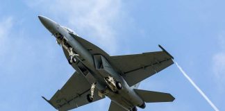 Parts Shortages Cripple America’s War Planes Jet flying in cloudy blue sky overhead view