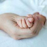 Adult hand holding a babys hand tightly