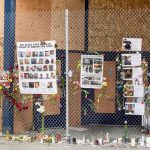 A memorial display with photos and flowers on a fence