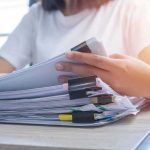 Court Twist Lets USPS Police Ballots Person organizing a stack of documents with binder clips
