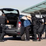 Homicide Ruling, Then… Salt Bags? customs officers detain a person beside a car with its trunk open
