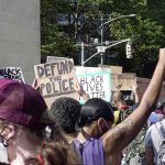 Residents Trapped As City Aids Encampment crowd at a protest holding signs and raising fists