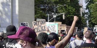 Residents Trapped As City Aids Encampment crowd at a protest holding signs and raising fists