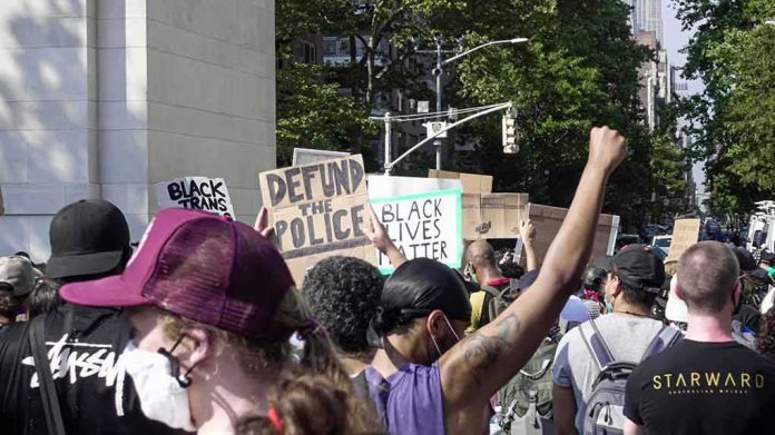 shutterstock_1754395223 crowd at a protest holding signs and raising fists