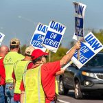 Monitor Flags Fain — Then DOJ Moves Workers holding blue strike signs along a roadside