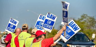 Monitor Flags Fain — Then DOJ Moves Workers holding blue strike signs along a roadside