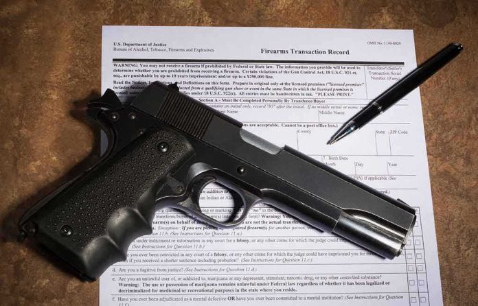 shutterstock_1026045637 Handgun on a firearms transaction form with a pen