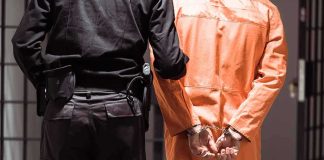 U.S. Marine Hospitalized — Russia Blocks Access Prisoner in orange jumpsuit handcuffed with guard standing beside