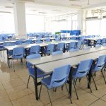 Empty cafeteria with rows of blue chairs and long tables