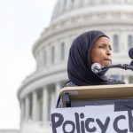 Every Muslim Smear—Backlash Erupts Fast Woman in hijab speaking at podium with microphones outside a domed building