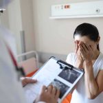 Barely There, Then Bone Spread Woman covering her face while doctor holds a clipboard in a hospital room