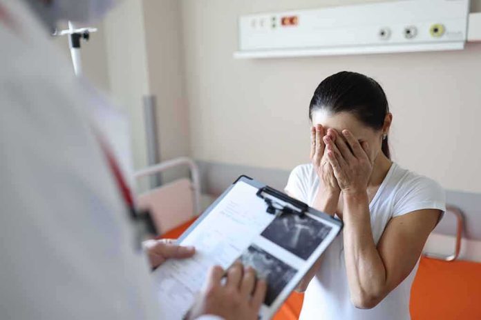shutterstock_2040259901 Woman covering her face while doctor holds a clipboard in a hospital room