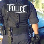 Shots Rip Columbia Park—Officer Falls Police officer in tactical vest standing by patrol car