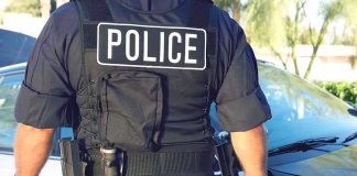 Shots Rip Columbia Park—Officer Falls Police officer in tactical vest standing by patrol car