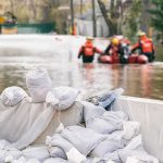 Record Crests, Deadly Rescues — Indiana Reels Sandbags stacked near a flooded street with rescue workers in a boat