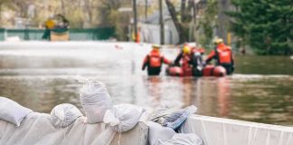 Record Crests, Deadly Rescues — Indiana Reels Sandbags stacked near a flooded street with rescue workers in a boat