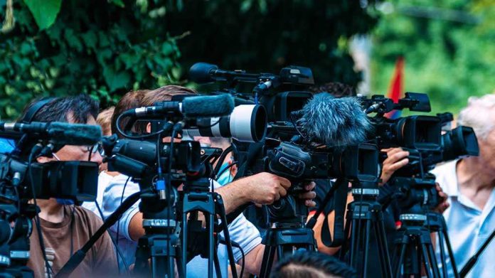 TV news cameras crowding together at an outdoor event
