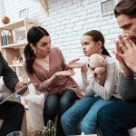 Family and counselor in tense discussion with upset child holding teddy bear