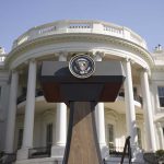 Press podium with presidential seal in front of the White House