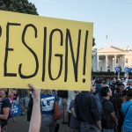 Hidden Influence: Israel Behind War Moves? Merle Wasmuth at protest holding large yellow 'RESIGN!' sign near the White House