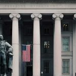 Statue in front of a neoclassical government building with columns and a U.S. flag