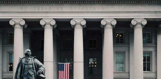 A Former CIA Official Had 303 Gold Bars At Home Statue in front of a neoclassical government building with columns and a U.S. flag