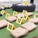 Evidence markers with wrapped packages, tire, and handgun at a crime scene