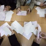 Hands counting paper ballots on a wooden table