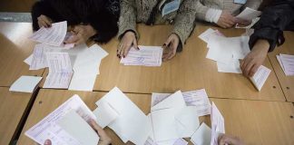 Hands counting paper ballots on a wooden table