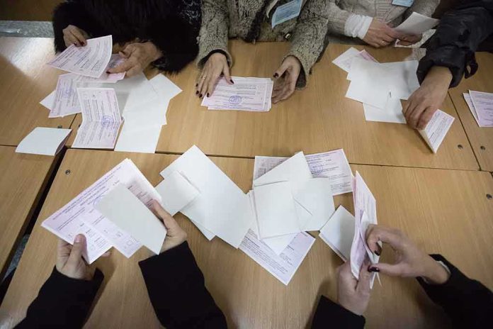 Hands counting paper ballots on a wooden table