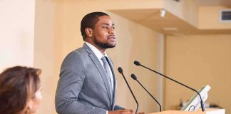 Man in suit speaking at a podium with microphones