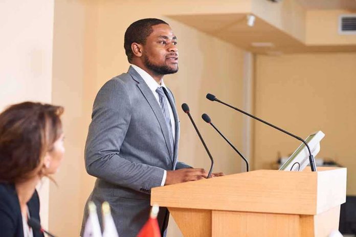 shutterstock_1432233818 Man in suit speaking at a podium with microphones