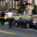 Police at urban street crime scene with yellow tape around parked cars